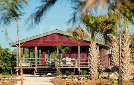 Een houten vakantiewoning tussen de palmbomen met rode gevelbekleding